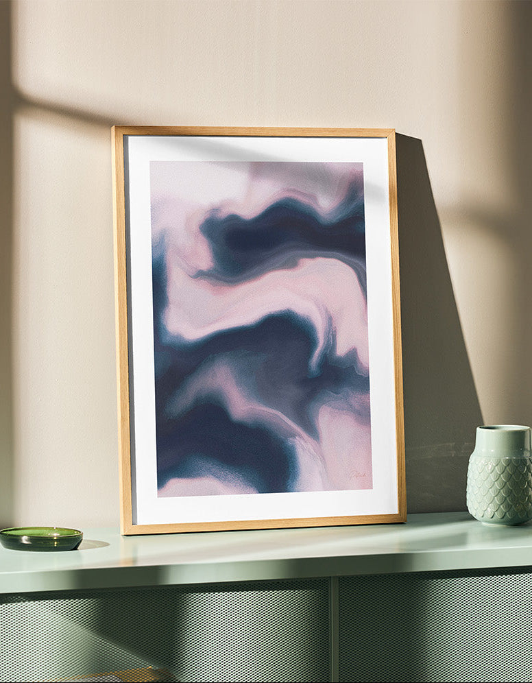 Framed contemporary abstract artwork "Soft Admission" from the Infinite Studio series by artist Nicole Potrich featuring blush and slate tones with fluid marble-inspired abstraction and layered texture. leaning on wall on top of a teal cupboard.